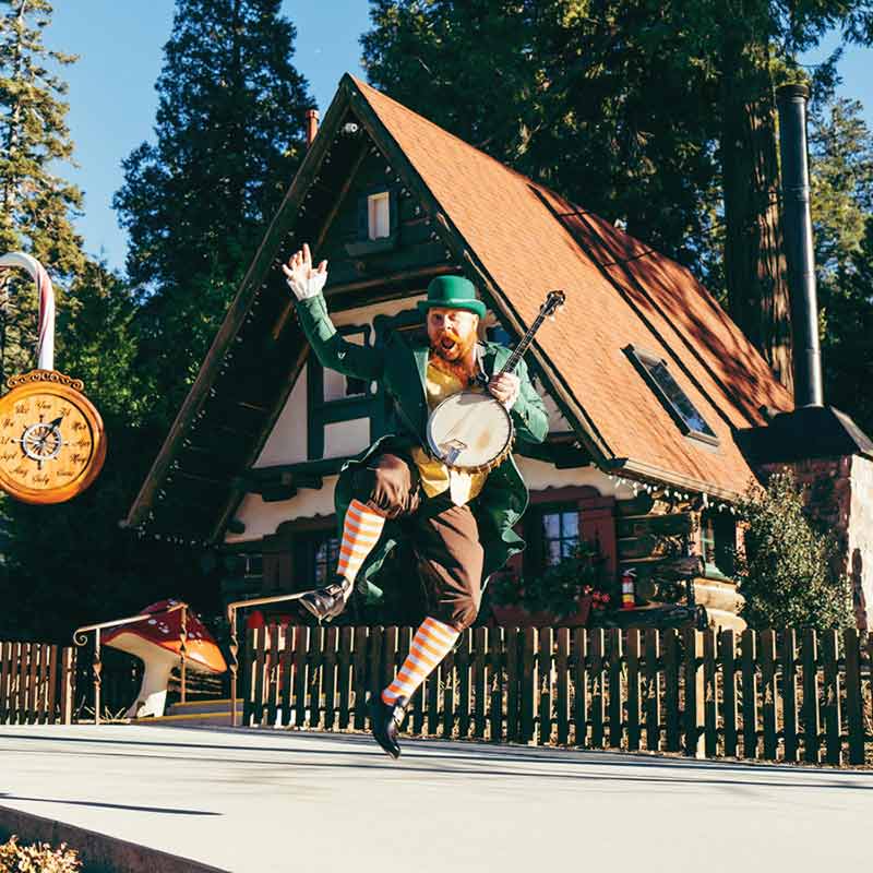 Shamrock4 Seamus the Leprechaun leaps into the air while holding a banjo during Shamrocks & Shenanigans.